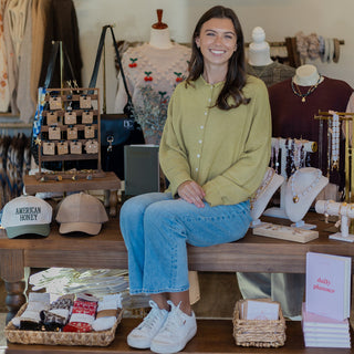 Woman sitting on a wooden table in a store with various items around her