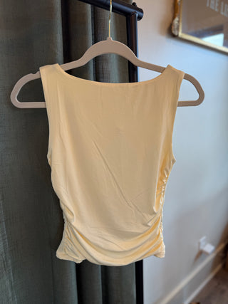 Butter yellow tank top hanging on a hanger against a neutral background