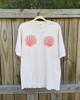 White t-shirt with pink shell designs hanging on a wooden fence