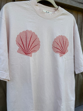 White t-shirt with red shell designs on a wooden surface